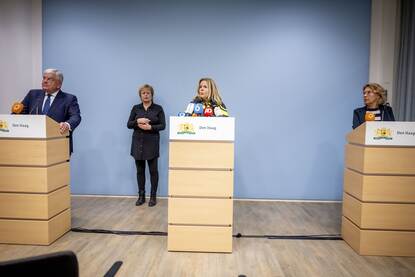 Een staande persconferentie in Den Haag, met de burgemeester links, de chef van de politie in het midden en de officier van justitie rechts. Op de achtergrond staat een gebarentolk.