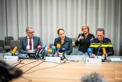 Een persconferentie in Rotterdam, met zittend in het midden de burgemeester Carola Schouten en aan haar zijden de officier van justitie en het hoofd van de Rotterdamse politie. Op de achtergrond een tolk gebarentaal, die zit.